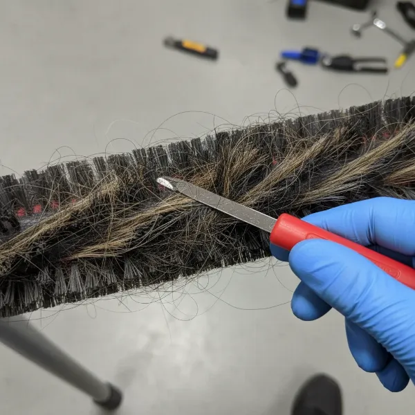 A person using a seam ripper to cut tangled hair from a vacuum brush roll