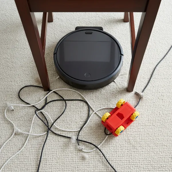 Robot vacuum stuck under a chair with cables and toys nearby, illustrating common obstructions
